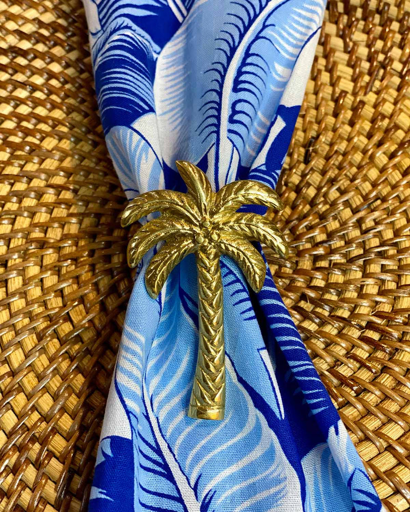 Brass palm tree napkin ring holding a white ginger palm leaf napkin.