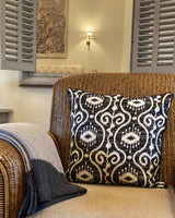 Black and white batik patterned cushion cover, pictured on rattan chair.
