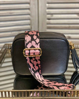 Black tassel bag with a pink animal print bag strap going across it. On a mirrored table.