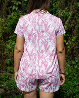 Woman wearing sleep accessories a matching shirt style top and shorts. Printed in a Balinese pink leaf print.