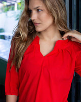 Close up of woman in poppy red top with a 3/4 sleeve and cuffed v neck.