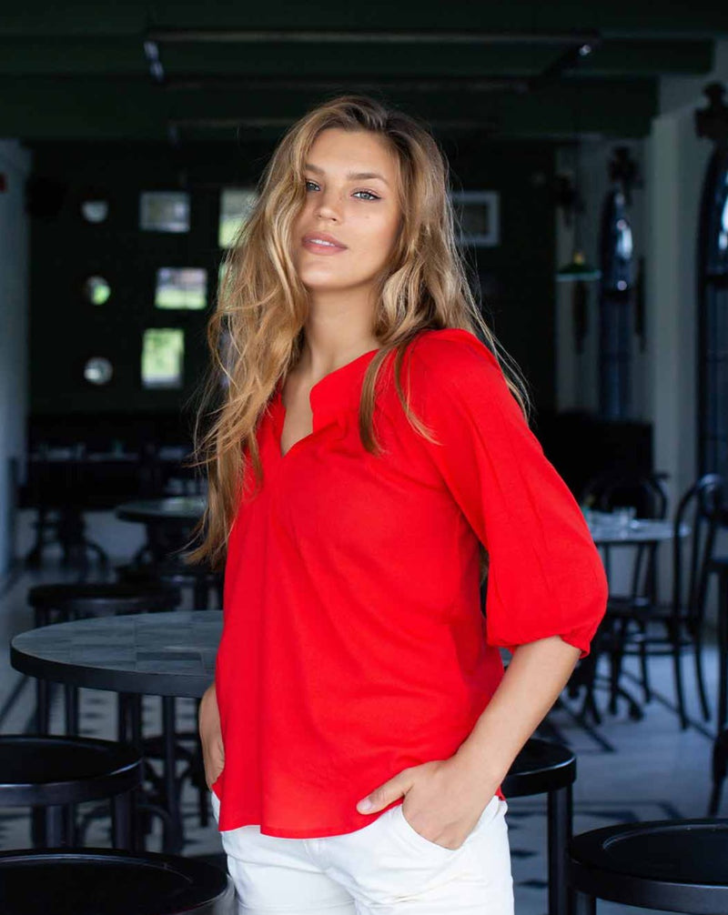 Woman posing in poppy red top with a 3/4 sleeve and cuffed v neck.