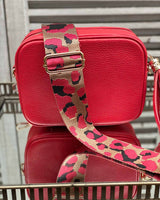 Red tassel bag with a red/beige cheetah print bag strap going across it. On a mirrored table.