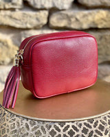 Burgundy leather rectangle bag with side tassel on a gold side table.