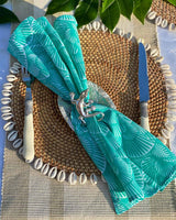 Turquoise seashell print napkin on rattan shell placemat with silver gecko napkin ring.