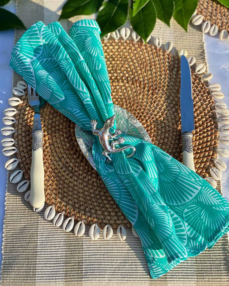 Set of four napkins printed with turquoise seashell print, on rattan shell placemat.