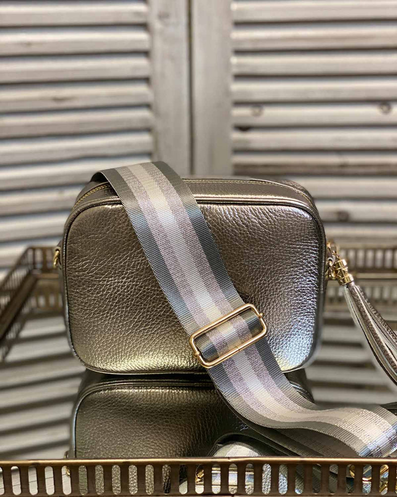 Gun metal tassel bag with grey/silver stripe bag strap going across it. On a mirrored table.