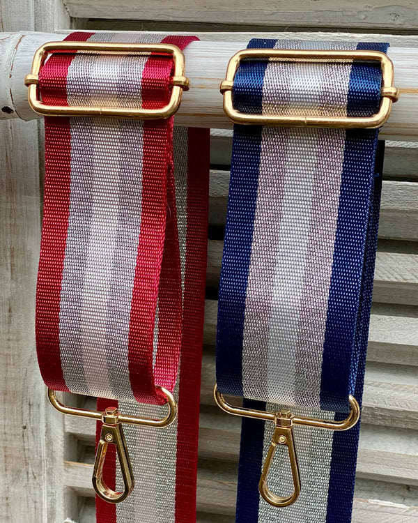 Two bag straps showing attachments, one with red/silver stripe and one with navy/silver stripe.