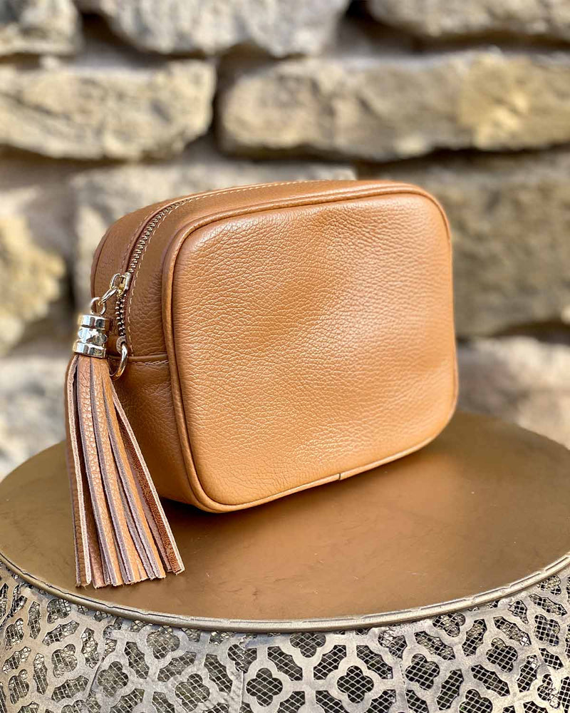Tan leather rectangle bag with side tassel on a gold side table.