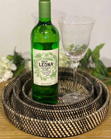 One small, one medium and one large woven black round rattan tray. Pictured with wine glass and bottle of wine.
