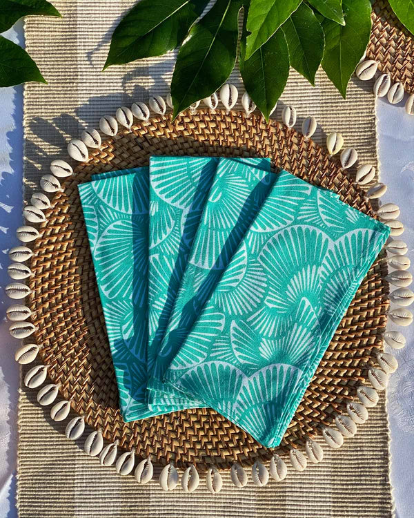 Set of four napkins printed with turquoise seashell print, on rattan shell placemat.