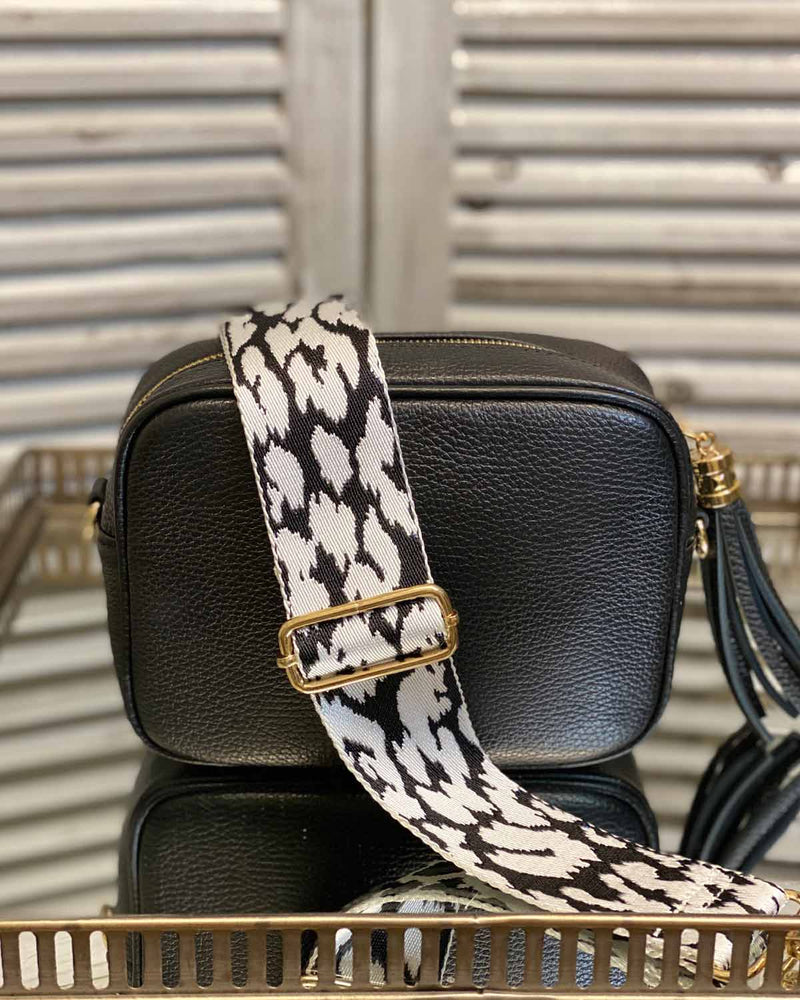 Black tassel bag with a black/white animal print bag strap going across it. On a mirrored table.
