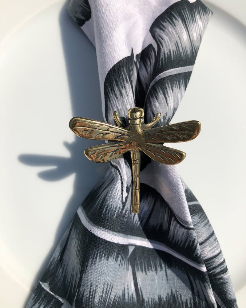 Brass dragonfly napkin ring with a grey banana leaf napkin.