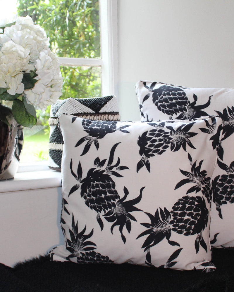 Two cushion covers printed with black pineapples on white cotton fabric. 