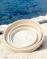 Small, Medium and Large white rattan trays pictured on a beach.