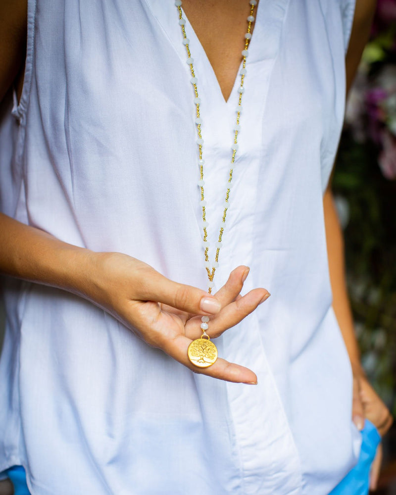 Woman holding a white crystal necklace with a tree of life pendant, with white shirt.